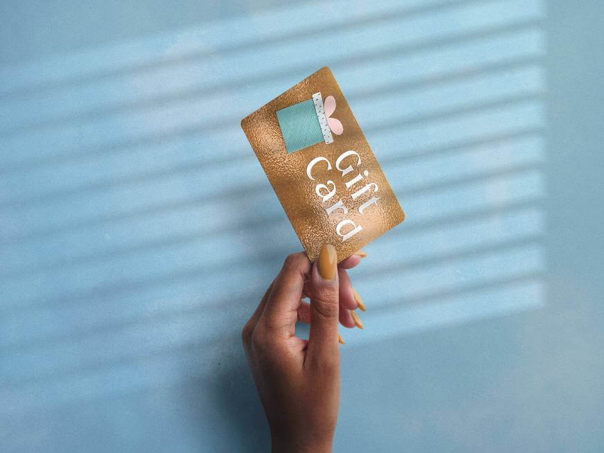 Woman holding a brown Gift Card up against a blue wall.
