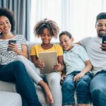 Mother, daughter, son and father using digital devices while sitting on a sofa.