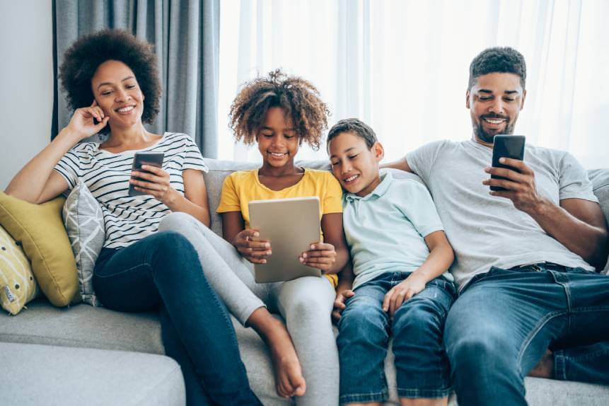 Mother, daughter, son and father using digital devices while sitting on a sofa.