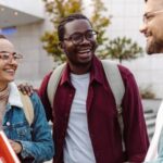 A group of 3 college students talking in front of a campus building.