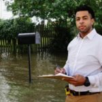 Man in white shirt holding clipboard in flooded natural disaster.