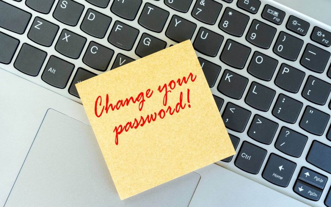 The words change passwords written on a yellow sticky note placed on a computer keyboard.